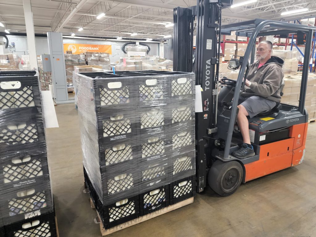 man uses a forklift to load pallets of milk