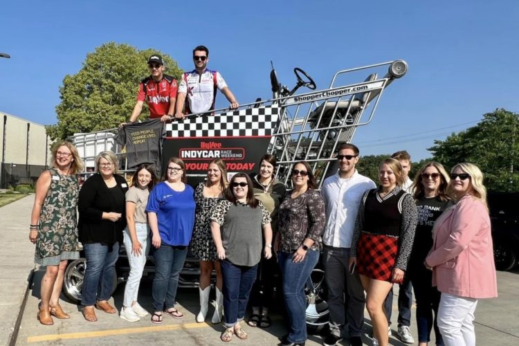 Food bank staff posing for a photo with Hy-Vee's giant shopping cart.